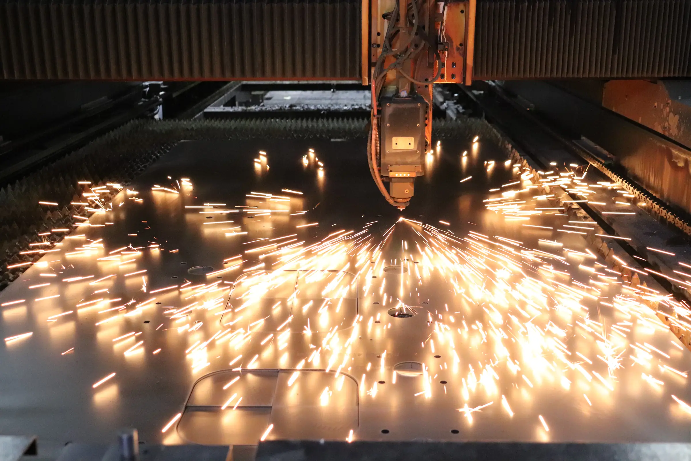 Fibre laser cutting a steel plate, glowing sparks across the bed
